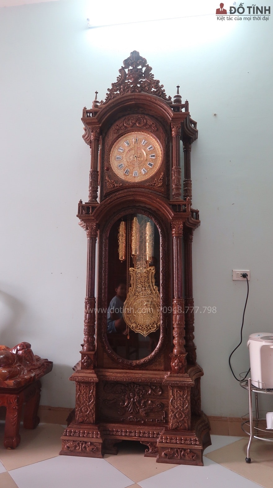 Chiếc đồng hồ cây gỗ mun đuôi công được phản chiếu dưới ánh đèn típ sáng loáng hiện lên những nét đẹp chạm trổ tinh anh - Ảnh: Internet